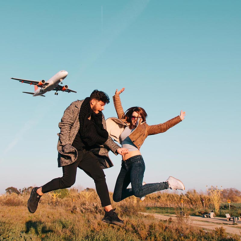 couple jumping for joy, airplane flying overhead
